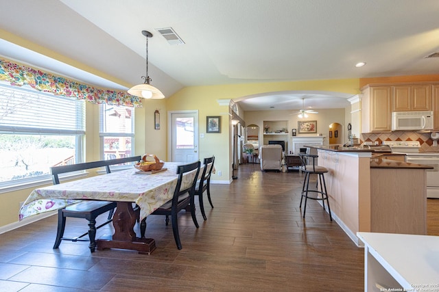 dining area with arched walkways, dark wood-type flooring, a fireplace, visible vents, and vaulted ceiling