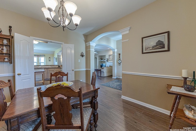 dining space featuring arched walkways, a chandelier, wood finished floors, baseboards, and decorative columns