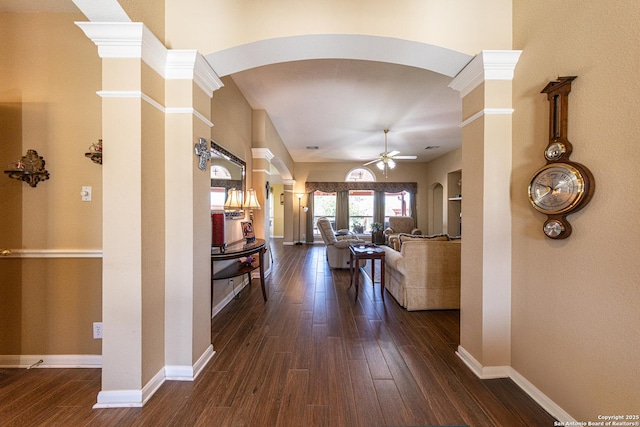 hallway with arched walkways, a high ceiling, dark wood-style flooring, and baseboards