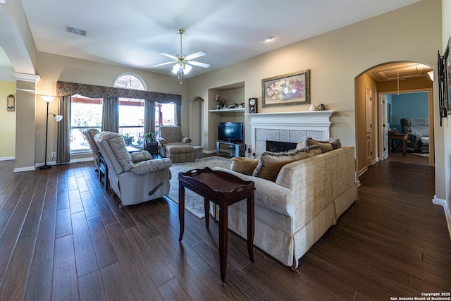 living room featuring dark wood-style floors, arched walkways, a fireplace, visible vents, and baseboards