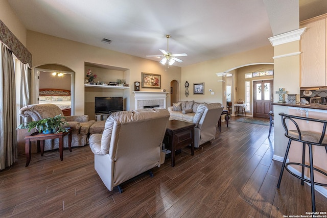 living room featuring arched walkways, a fireplace, visible vents, dark wood-type flooring, and a ceiling fan