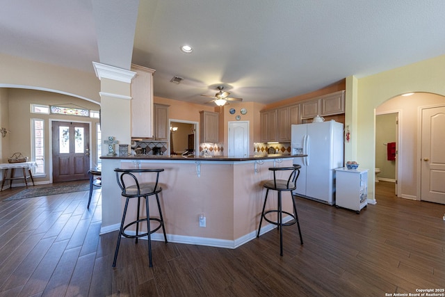 kitchen with white fridge with ice dispenser, a breakfast bar, arched walkways, and dark countertops