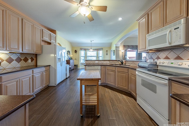 kitchen with white appliances, dark countertops, a peninsula, light brown cabinetry, and a sink