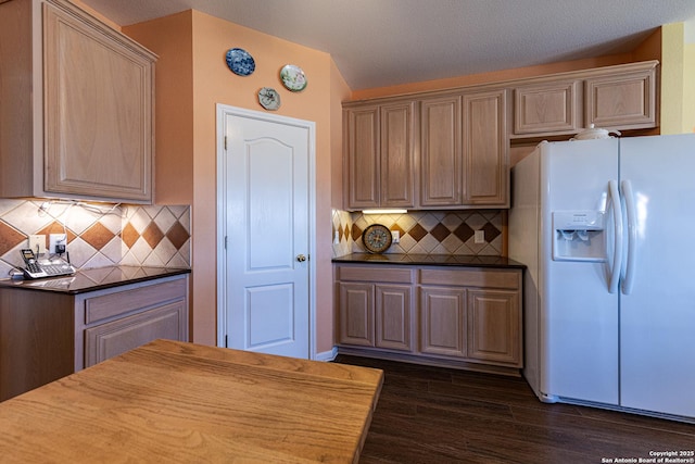 kitchen with dark countertops, white refrigerator with ice dispenser, decorative backsplash, and dark wood-style flooring