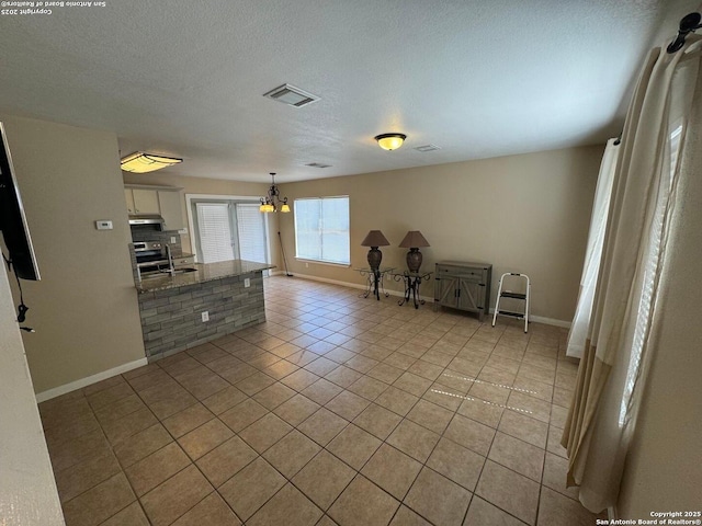 interior space featuring light tile patterned floors, a textured ceiling, a chandelier, visible vents, and baseboards