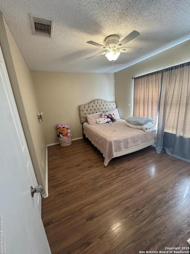 bedroom featuring a textured ceiling, wood finished floors, visible vents, baseboards, and a ceiling fan