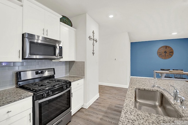 kitchen with decorative backsplash, light wood-style flooring, appliances with stainless steel finishes, light stone countertops, and a sink