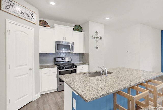 kitchen with light stone counters, light wood finished floors, appliances with stainless steel finishes, a sink, and a kitchen bar