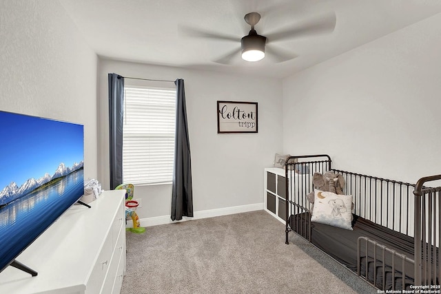 carpeted bedroom with a nursery area, a ceiling fan, and baseboards