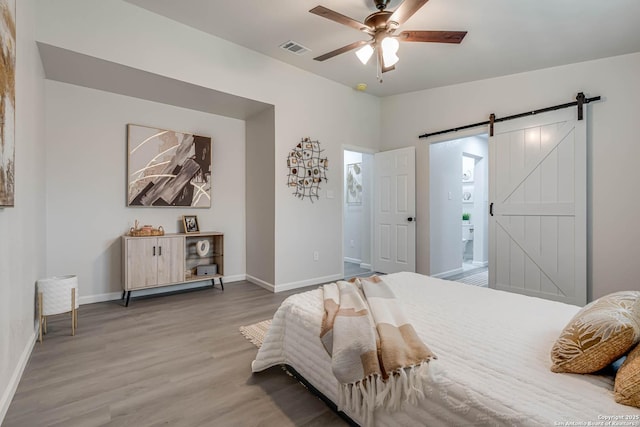 bedroom featuring a barn door, wood finished floors, visible vents, and baseboards