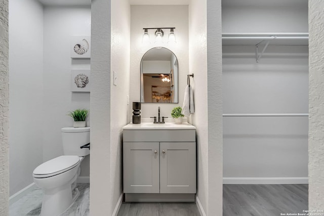 bathroom with a walk in closet, baseboards, vanity, and toilet