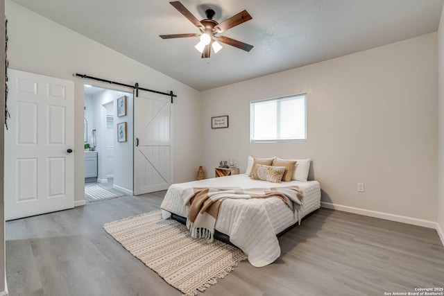 bedroom featuring ensuite bathroom, a barn door, baseboards, vaulted ceiling, and light wood finished floors