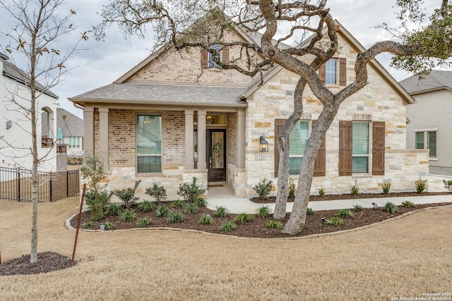 french country home with brick siding, stone siding, fence, and roof with shingles