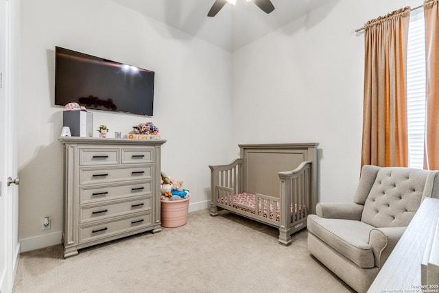 bedroom featuring light colored carpet, ceiling fan, a crib, and baseboards