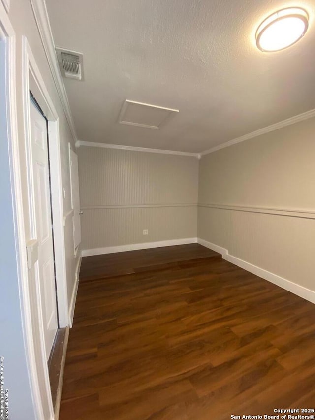 unfurnished room with visible vents, ornamental molding, wainscoting, dark wood finished floors, and attic access