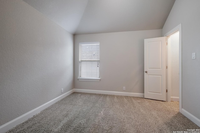 empty room featuring lofted ceiling, light carpet, and baseboards