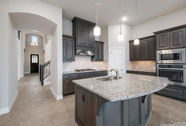 kitchen with arched walkways, stainless steel appliances, a sink, a towering ceiling, and range hood