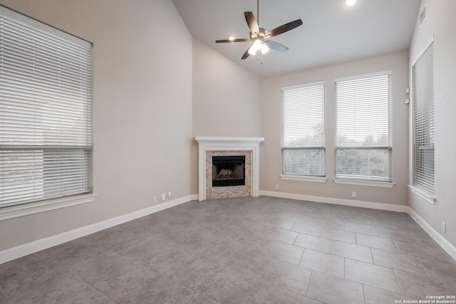 unfurnished living room with ceiling fan, a tile fireplace, lofted ceiling, and baseboards