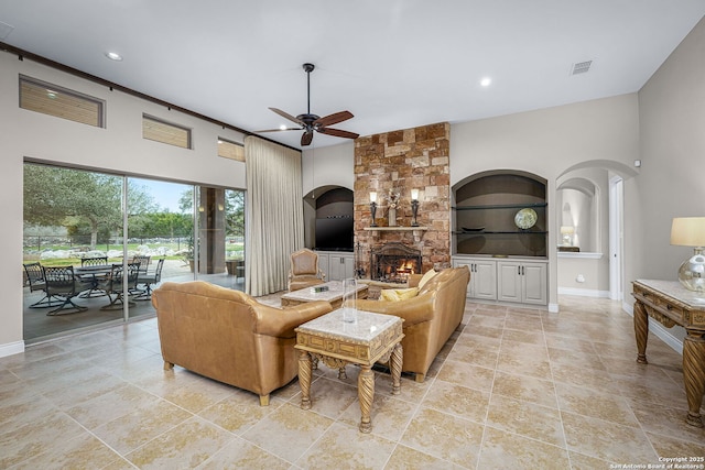 living area with built in shelves, arched walkways, a fireplace, visible vents, and a ceiling fan