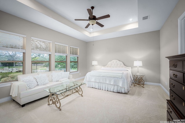 bedroom with baseboards, visible vents, a tray ceiling, and light colored carpet