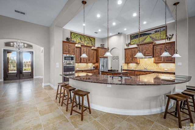 kitchen featuring visible vents, a towering ceiling, a breakfast bar area, a large island with sink, and a sink