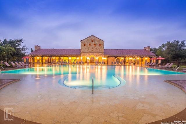 pool at dusk featuring a patio area and a community pool