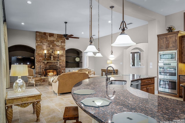 kitchen with visible vents, dark stone counters, stainless steel appliances, a fireplace, and a sink