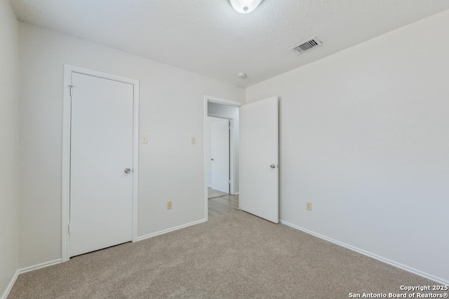 unfurnished bedroom featuring baseboards, visible vents, a textured ceiling, and light colored carpet