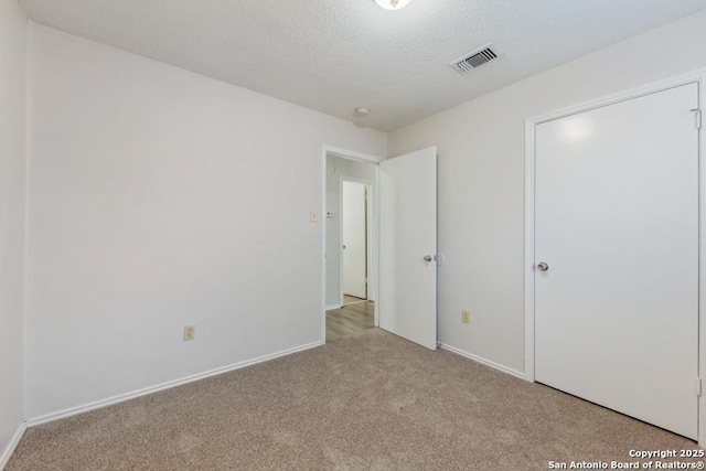 unfurnished bedroom featuring light carpet, a textured ceiling, visible vents, and baseboards