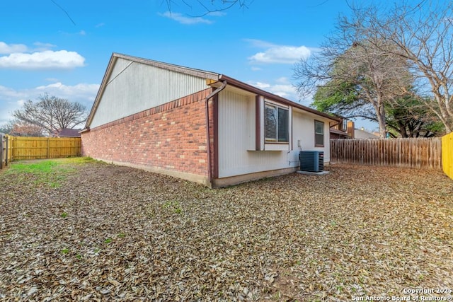 view of side of home featuring central AC, brick siding, and a fenced backyard