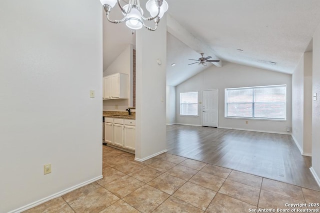 interior space featuring light tile patterned floors, baseboards, lofted ceiling with beams, a sink, and ceiling fan with notable chandelier