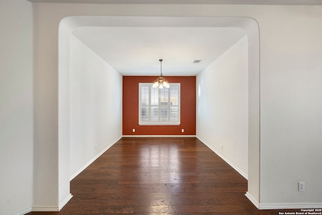 spare room with baseboards, visible vents, a chandelier, and wood finished floors