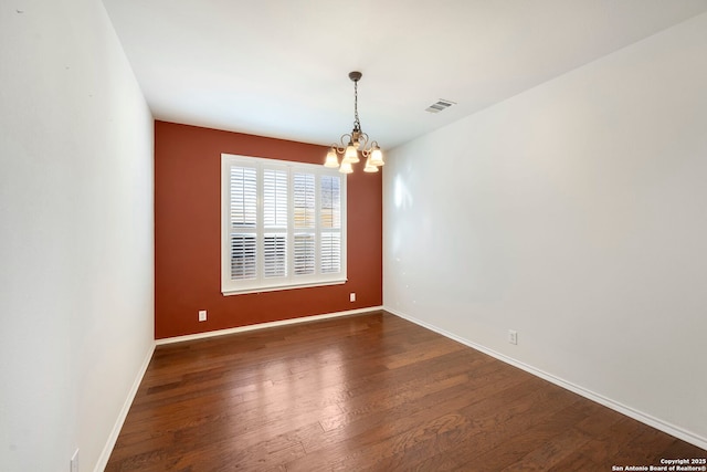 spare room with visible vents, a notable chandelier, baseboards, and wood finished floors