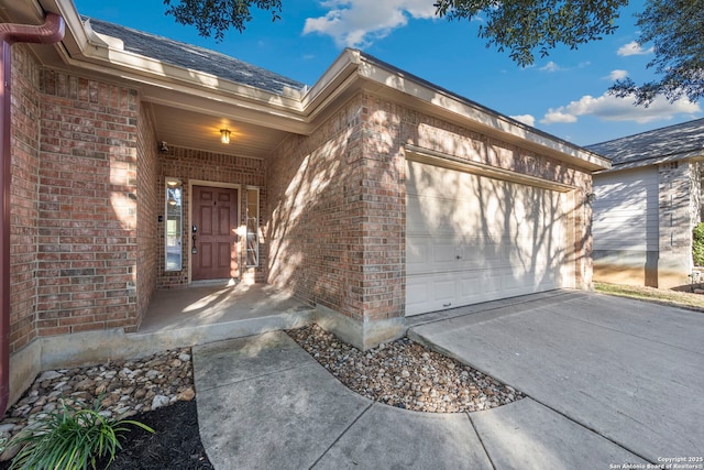 view of exterior entry featuring a garage, driveway, and brick siding