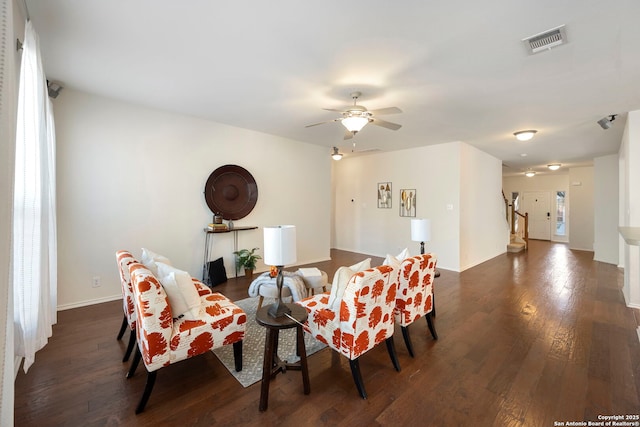 living area featuring dark wood-style flooring, visible vents, a ceiling fan, baseboards, and stairs