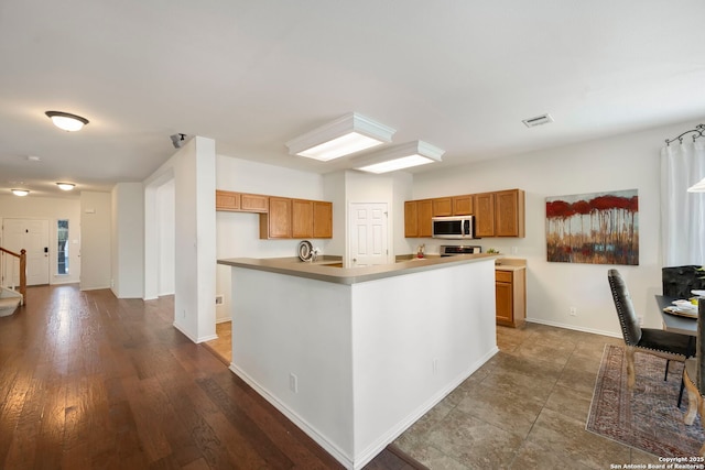 kitchen with stove, baseboards, brown cabinetry, a center island, and stainless steel microwave