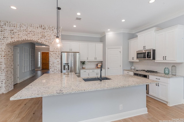 kitchen featuring arched walkways, a sink, appliances with stainless steel finishes, a large island, and light wood-type flooring