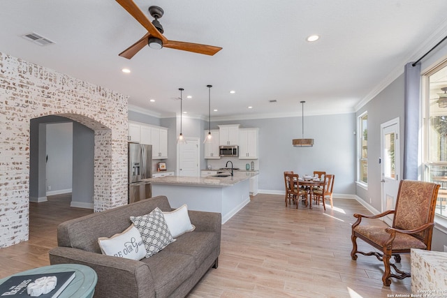 living room featuring light wood-style floors, arched walkways, visible vents, and crown molding