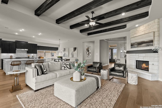 living room with a fireplace, a ceiling fan, wood finished floors, beamed ceiling, and baseboards