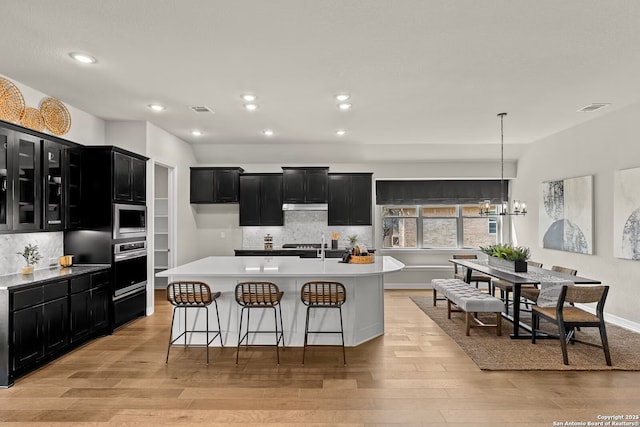 kitchen featuring visible vents, light wood-style flooring, stainless steel appliances, dark cabinetry, and under cabinet range hood