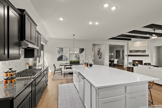 kitchen featuring light wood-style flooring, a fireplace, stainless steel gas cooktop, and backsplash