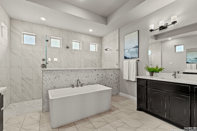 bathroom featuring marble finish floor, a walk in shower, a soaking tub, and vanity