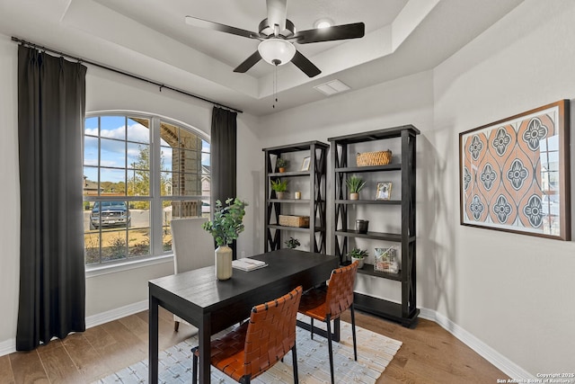 office area with light wood finished floors, baseboards, a raised ceiling, and a ceiling fan