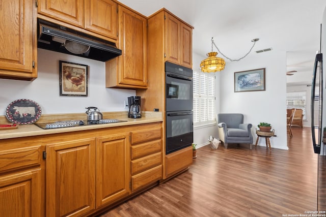 kitchen with dobule oven black, under cabinet range hood, visible vents, light countertops, and cooktop