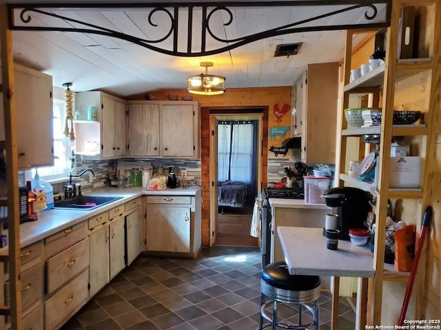 kitchen with dark tile patterned flooring, vaulted ceiling, light countertops, stainless steel range with gas cooktop, and a sink