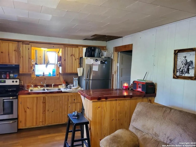 kitchen featuring a breakfast bar area, appliances with stainless steel finishes, dark wood-type flooring, wooden counters, and a sink