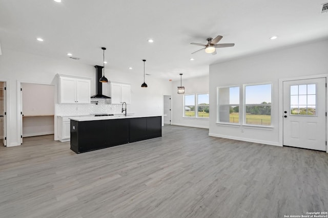 kitchen featuring light wood finished floors, tasteful backsplash, light countertops, white cabinetry, and wall chimney range hood