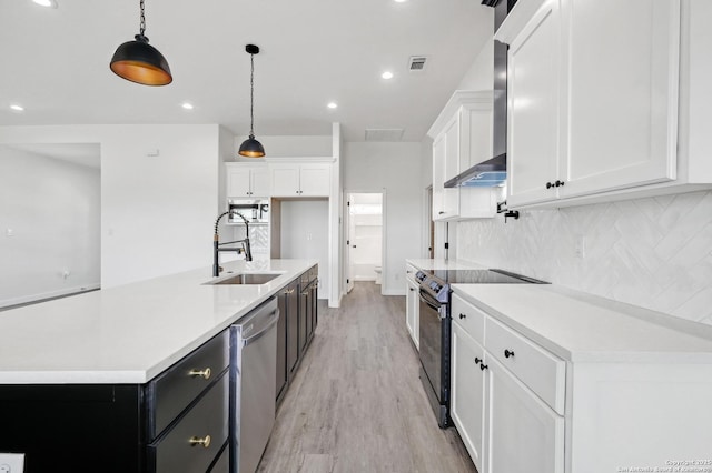 kitchen with a sink, white cabinets, wall chimney range hood, appliances with stainless steel finishes, and tasteful backsplash