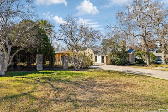 view of property hidden behind natural elements with concrete driveway, a front lawn, and a fenced front yard