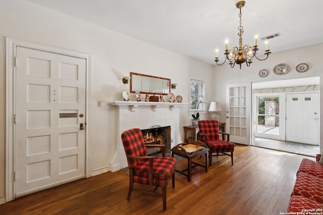 living area featuring visible vents, a fireplace, a notable chandelier, and hardwood / wood-style floors